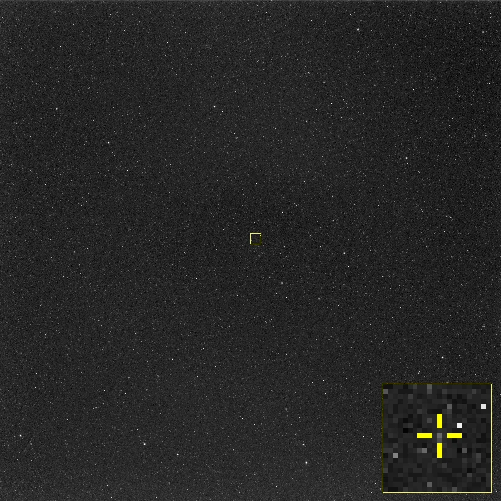 A square, grainy black-and-white star field with a small yellow box drawn around one faint point near the centre; an inset at the bottom right magnifies that box into coarse grey pixels with a yellow cross-hair marking the point