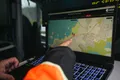Una mano señala la pantalla de un portátil con el SAS Monitoring Tool, un mapa de la costa de Andøya con dos marcadores de posición, uno E1 y otro E6, y una lectura de la distancia entre ambos