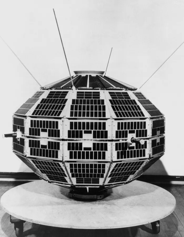 An exhibition unit of the Alouette satellite, shown by NASA in 1964: a faceted, flattened ball tiled with solar cells, its short antennas raised, on a wheeled stand.