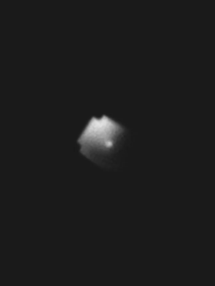 BlueWalker 3 seen from the ground through a telescope: its unfolded antenna array, a pale, blurred square against the black sky.