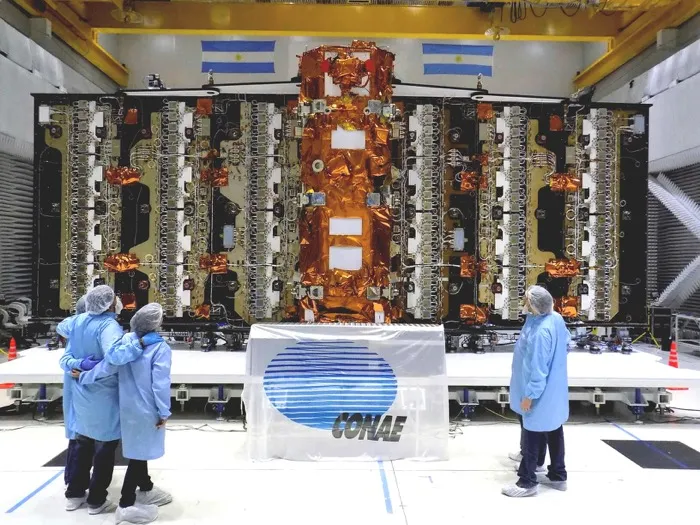 The SAOCOM 1A satellite in a test hall in Bariloche before its launch, its gold-foiled body upright at the centre of its unfolded radar antenna, technicians in clean-room suits looking on.