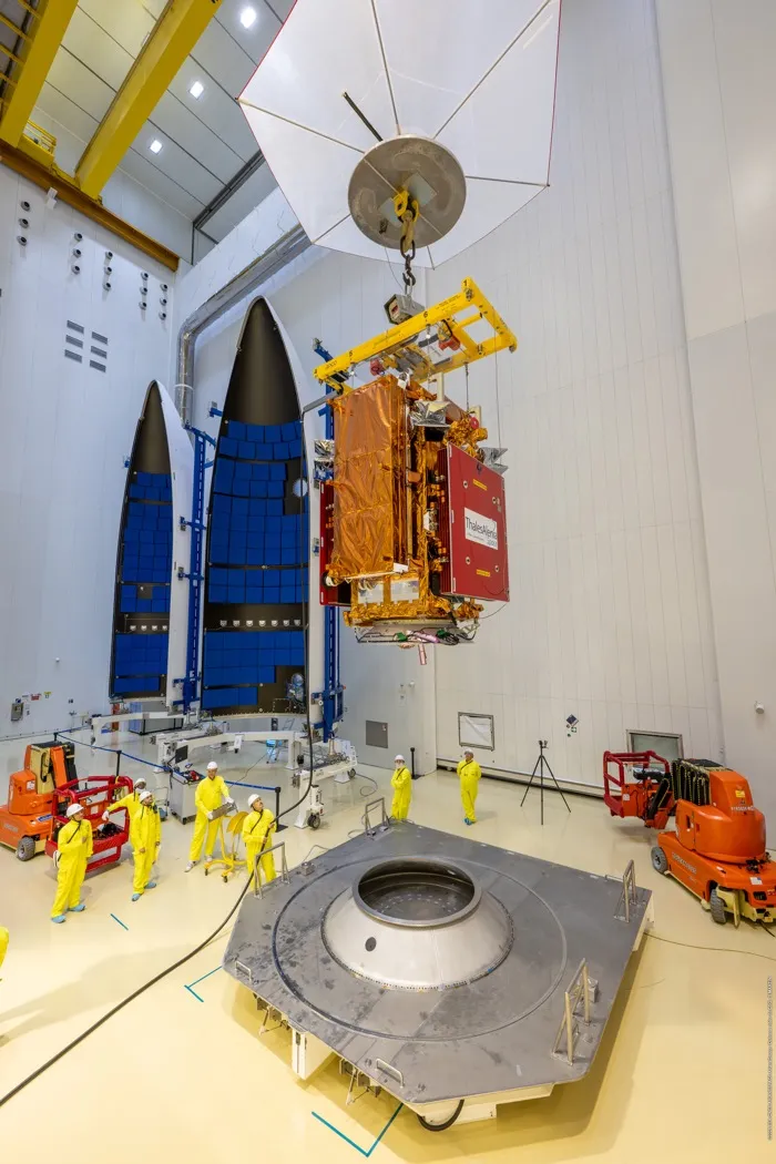 The Sentinel-1D spacecraft in its gold foil, hanging from a crane above its Ariane 6 launch adaptor in the clean room at Kourou in 2025, the two halves of the fairing behind it.